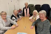 Aelodau o Merched y Wawr Bethel yn eistedd ar bwrdd yn barod i wneud y cwis